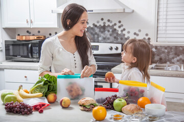 A young mother and daughter packs fresh fruit, vegetables and food into clear storage bags