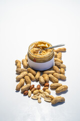 peanut butter in an open glass on a white background, next to scattered peanuts
