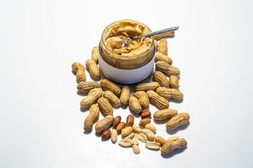 peanut butter in an open glass on a white background, next to scattered peanuts