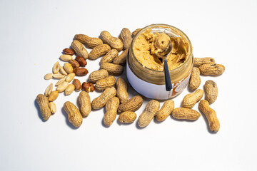 peanut butter in an open glass on a white background, next to scattered peanuts