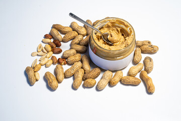 peanut butter in an open glass on a white background, next to scattered peanuts
