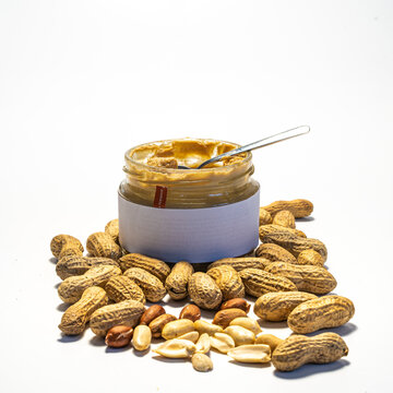 peanut butter in an open glass on a white background, next to scattered peanuts