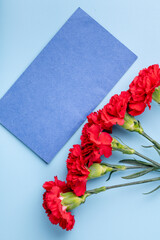 red carnation and blue envelope with space for text on a blue background, top view, festive background, postcard for defender of the fatherland day, women's day, March 8, mother's day