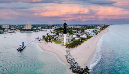 panoramic drone shot of sunset over city with lighthouse on beach and ocean