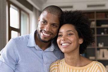 Handsome bearded husband and beautiful curly-haired wife standing in modern room smiling looking at camera, having wide toothy smile, African couple close up portrait. Love, romantic dating concept