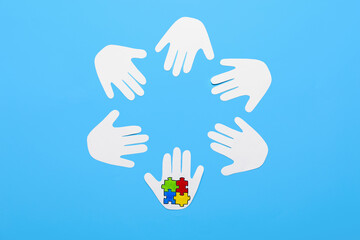 Paper human palms with colorful puzzle pieces on color background. Concept of autistic disorder