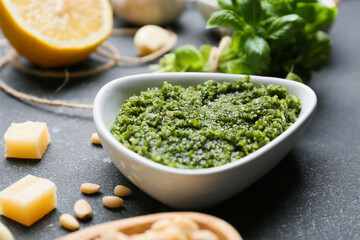 Bowl of tasty pesto sauce and ingredients on dark background