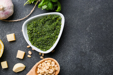 Bowl of tasty pesto sauce and ingredients on dark background