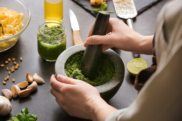 Woman making pesto sauce with mortar and pestle on table in kitchen