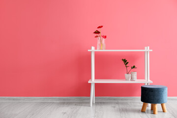 Vase with flowers, houseplant on shelf unit and pouf near color wall