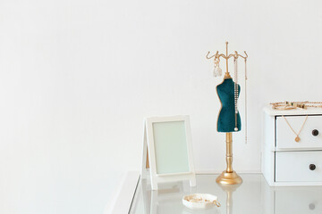 Different stylish jewelry and photo frame on glass table near light wall