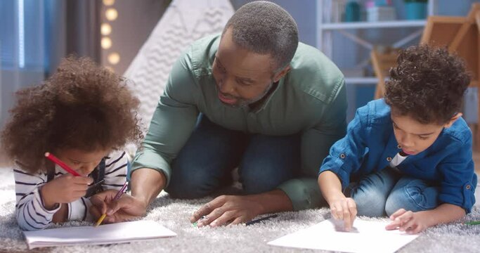 Close up of happy african american grandfather helping little grandchildren draw beautiful pictures to present to parents.