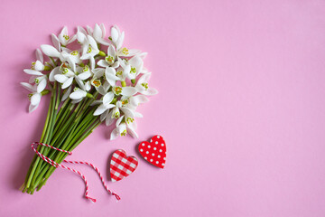 A bouquet of spring snowdrop flowers and red-white hearts on a pink background for the holiday of March 1, Valentine's Day.