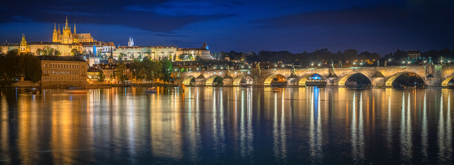 Astonishing panoramic view from a distance of the Prague Castle at night, showing the bridge's reflection.