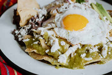 Mexican green chilaquiles with fried egg, chicken and spicy green sauce traditional breakfast in Mexico	
