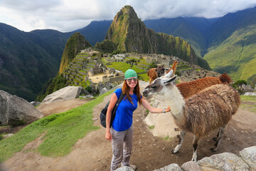 Young woman standing with friendly llamas at Machu Picchu overlook in Peru