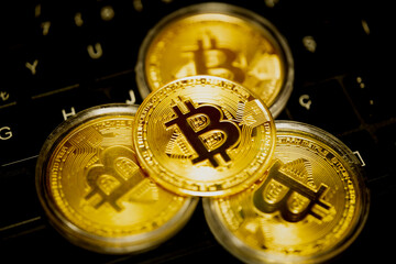 Symbolic gold bitcoin coins with bitcoin symbol on keyboard keys. Bitcoin coin in the middle in selective focus. Cryptocurrency, stock market, blockchain, digital money concept.