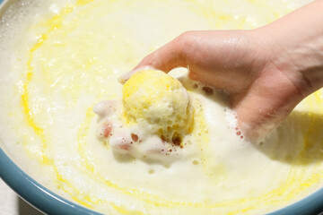 Female hand with dissolving bath bomb with bowl of water on light background, closeup