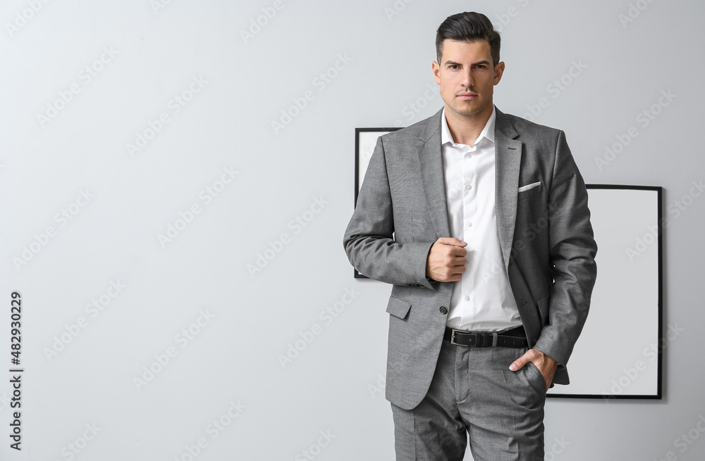 Wall mural Handsome man in formal suit posing near grey wall