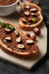 Board of bread with chocolate paste and hazelnuts on table, closeup