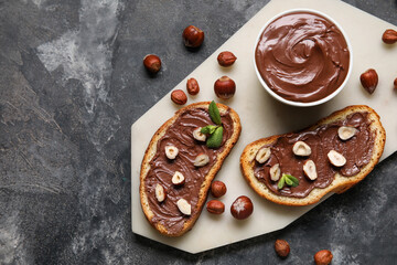 Board of bread with chocolate paste and hazelnuts on black background