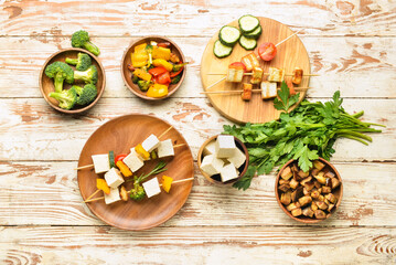 Composition with grilled tofu cheese skewers and vegetables on light wooden background