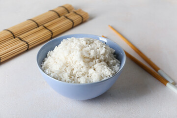 Bowl with tasty boiled rice and chopsticks on light background, closeup