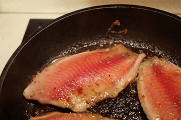 The process of frying tilapia fillets in a frying pan with spices.