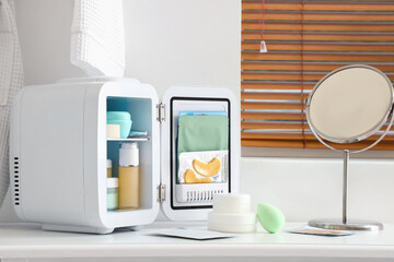 Small cosmetic refrigerator and mirror on dressing table near light wall