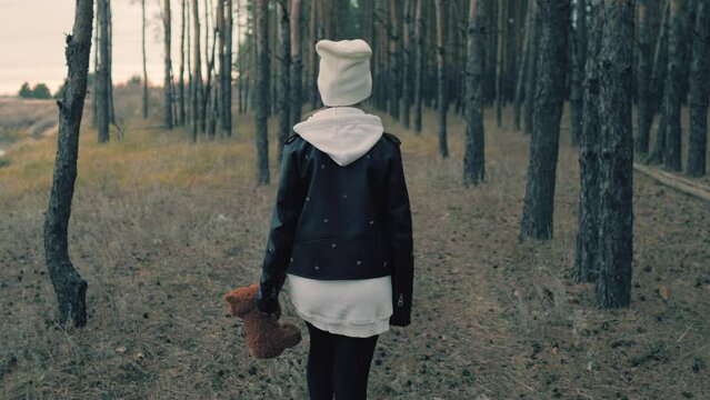 Sad depressed girl with teddy bear walking on a lonely road. Childhood. Education. Problem. Sad little girl and her teddy bear. Sad little girl feels lonely.