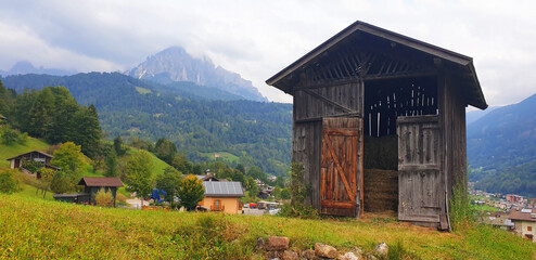 Landscape with a wooden hayloft against the backdrop of the village and the dolomite mountains.