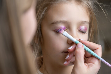 mom uses a brush to apply shiny shadows on eyelids of her daughter