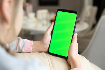 Little girl use smart phone with blank green screen mock up display for advertising text while rest on couch in living room at modern home. Phone with green screen and chroma key for copy space