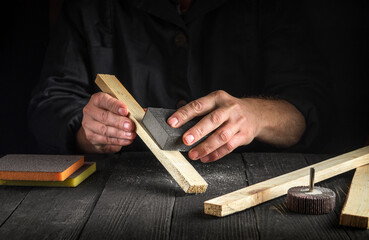 The craftsman cleans wood planks with an abrasive tools. Builder hands close up. Renovation or construction idea