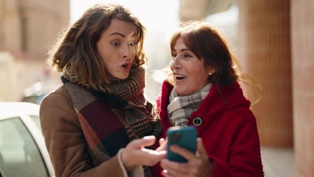 Mother and daughter smiling confident using smartphone at street