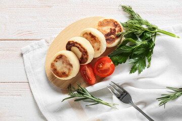 Board with tasty cottage cheese pancakes and tomato on light wooden background