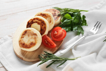 Board with tasty cottage cheese pancakes and tomato on light wooden background