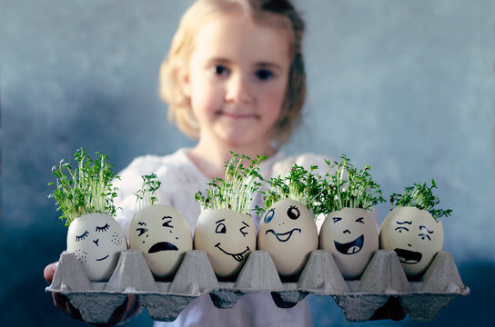 Easter eggs with faces with emotions and green herbal cress. Easter decoration on food and egg which are holding by little girl. Spring with fresh and healthy herbal. Portrait of child.