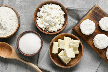 Bowl with cottage cheese and ingredients for preparing pancakes on grey background