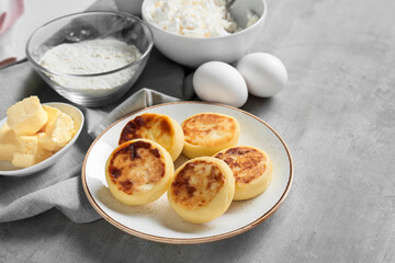 Plate with tasty cottage cheese pancakes and ingredients on grey background