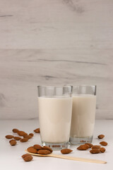 Two glasses with alternative dairy free almond milk and nuts on light background. Lactose free beverage