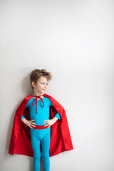 Little child play superhero. Dreamy boy in blue superhero costume and red cape