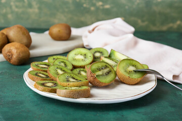 Plate with fresh cut kiwi on green background, closeup