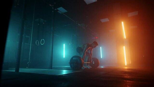 A strong man without a T-shirt with a naked torso Preparation and lifts a barbell over his head a barbell with a lot of weight in slow motion in colored light. Blue orange neon light in the gym