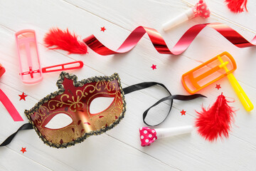 Carnival mask and rattles for Purim holiday with party decor on white wooden background