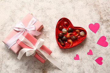 Heart shaped box with tasty chocolate candies and gifts on light background