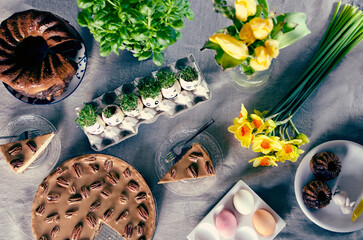 Easter table with delicious food, easter eggs with cress and daffodils. Plate of easter cake for dessert as a tradition for breakfast in holiday. Flat lay and top view. Beautiful composition on table.