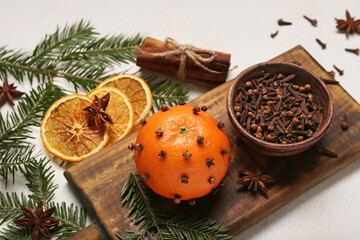 Handmade Christmas decoration made of tangerine with cloves and fir branches on light background, closeup