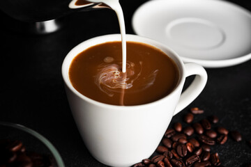 Coffee americano with milk in cup and saucer isolated on dark background. Hot coffee