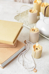 Stack of books with necklace and burning candles on white table